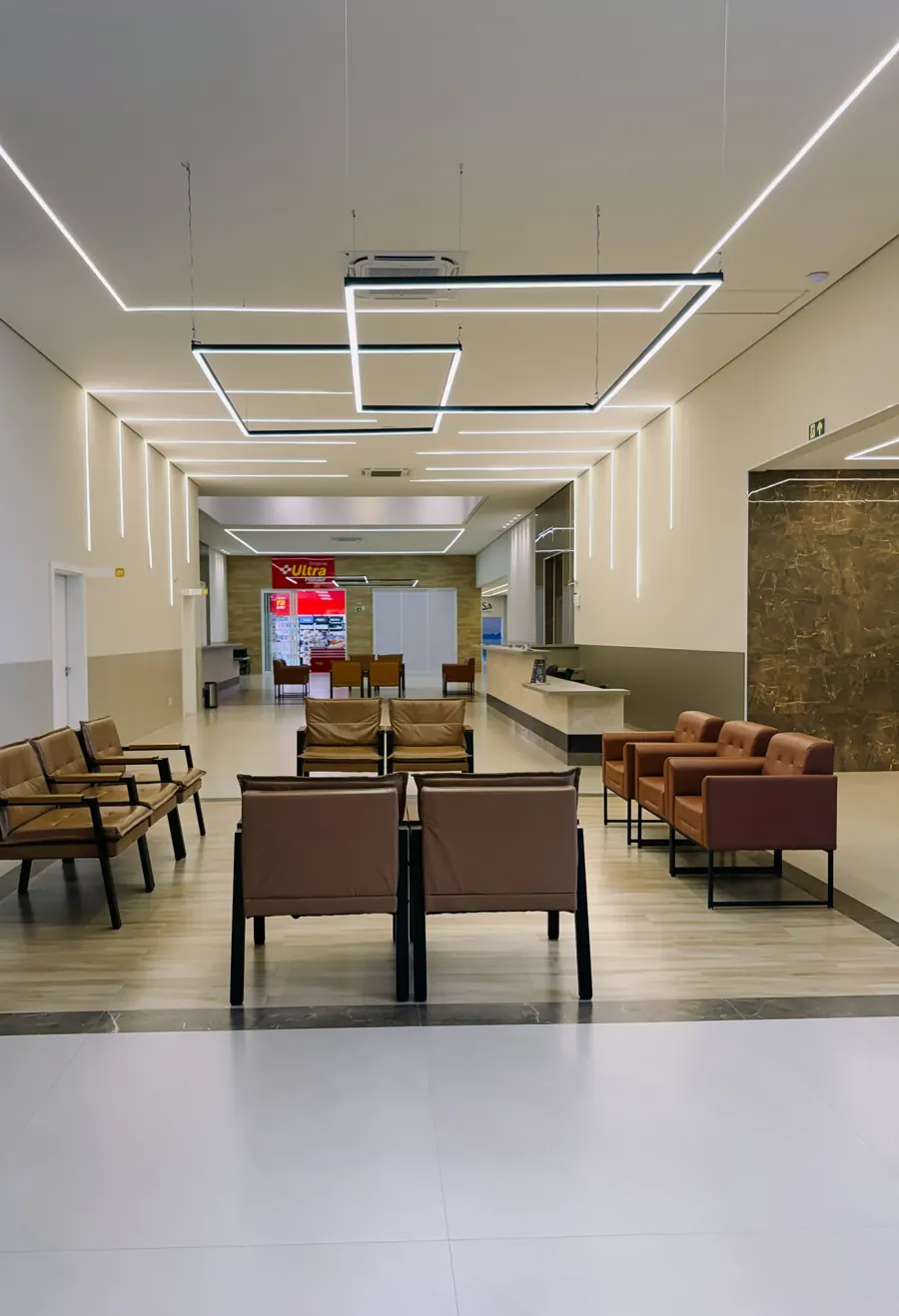 Área de espera do centro médico Aquarela Saúde, com poltronas em couro e iluminação em linhas